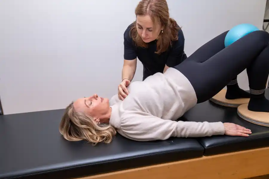 Galina Bell guiding a client through a Pilates bridge exercise with a ball between the knees